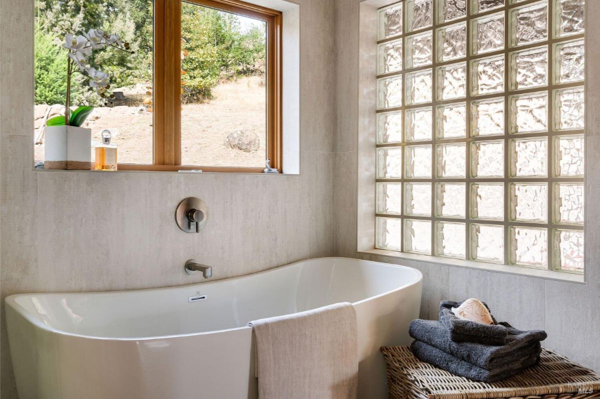 Freestanding bathtub next to a window and glass-block wall.
