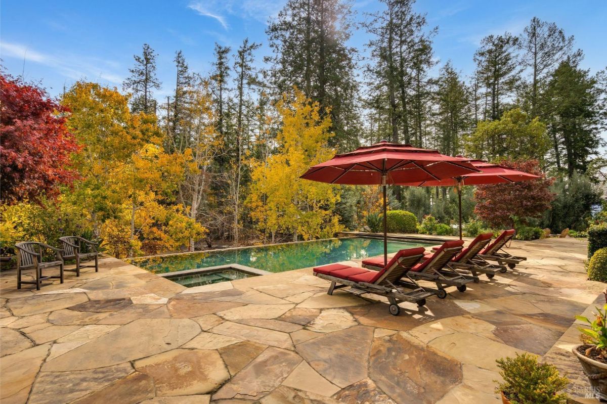 Stone patio with a swimming pool, surrounded by autumn trees and red lounge chairs.