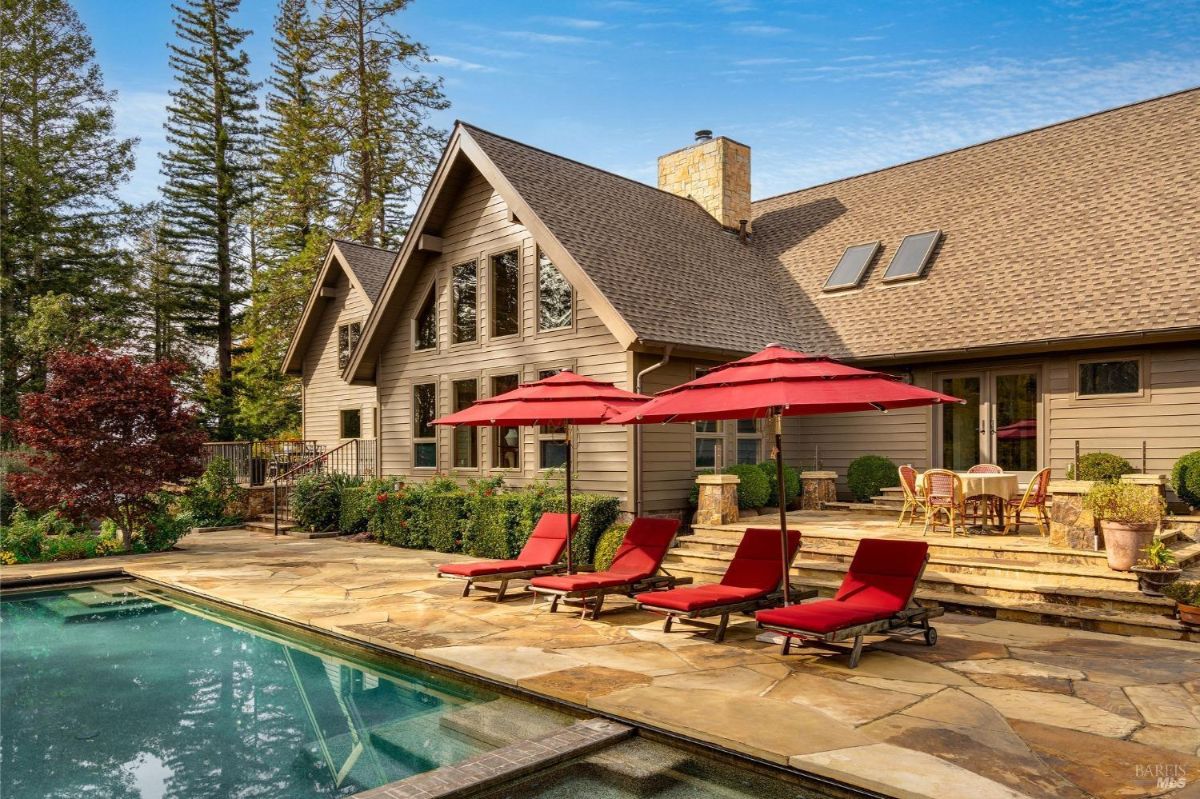 House with a large backyard featuring a swimming pool, patio, and red lounge chairs.