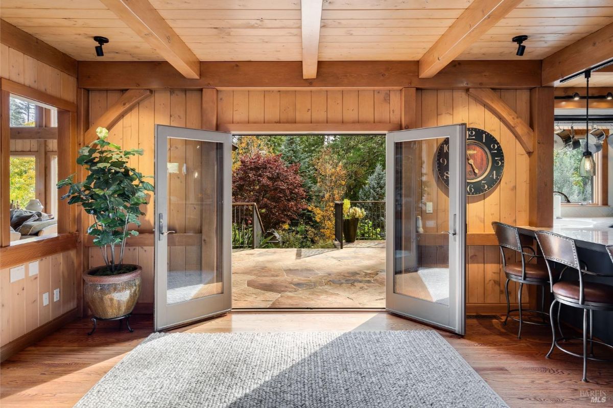 Open living area with double doors leading to a patio surrounded by trees.