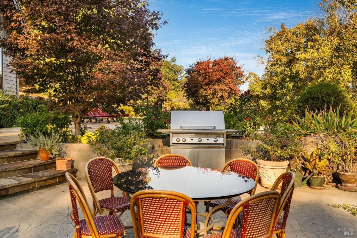 Outdoor patio area with a barbecue grill and dining table surrounded by colorful foliage.