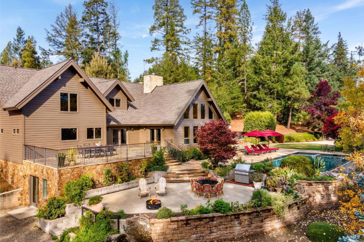 Large house with a spacious backyard featuring a patio, fire pit, dining area, swimming pool, and surrounded by trees.