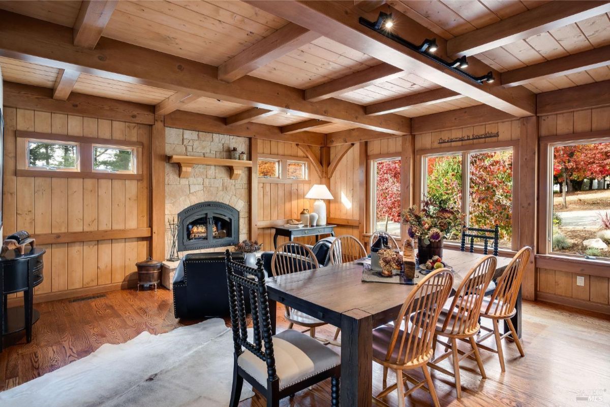 Wood-paneled dining room features a rustic fireplace and large windows with views of vibrant outdoor foliage.