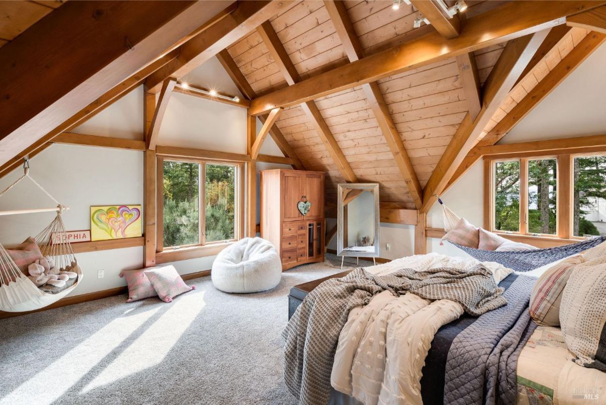 Bedroom with exposed wood beams, large windows, and cozy decor including a hammock and bean bag.