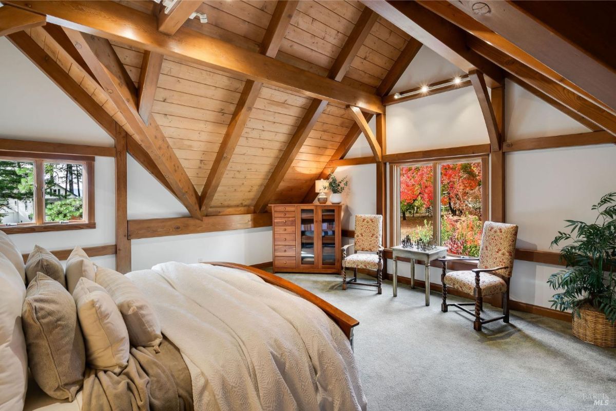Bedroom featuring wood beams, neutral tones, and a seating area with chairs and a small table near the window.
