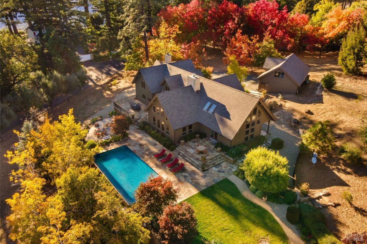 Aerial view of a house with a pool, patio area, and colorful landscaping.