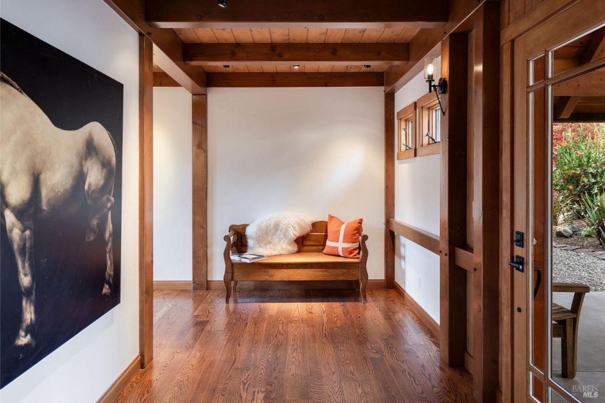 Hallway with a wooden bench, orange pillow, fur throw, and a view of the outdoor area through a glass door.