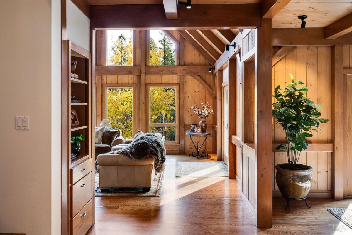 Interior view with wooden walls, large windows, and a sitting area with natural light.