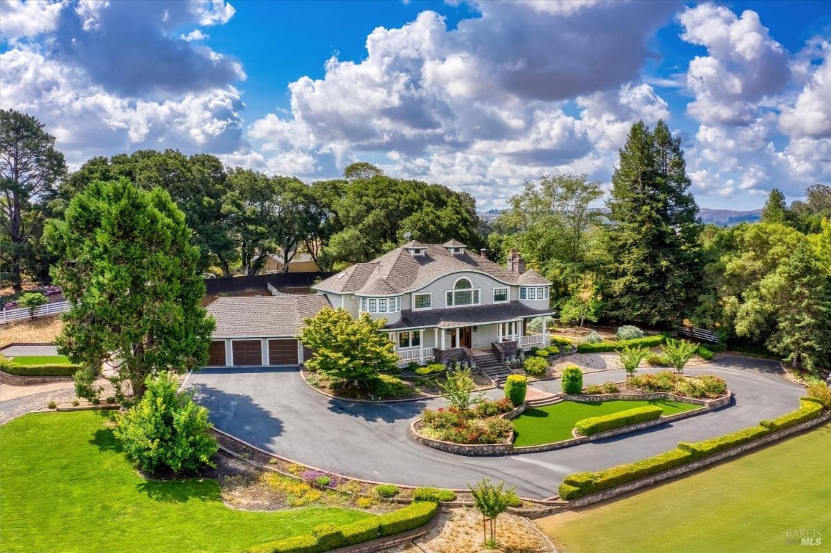 House with a circular driveway, landscaping, and surrounding trees, with distant hills visible in the background.