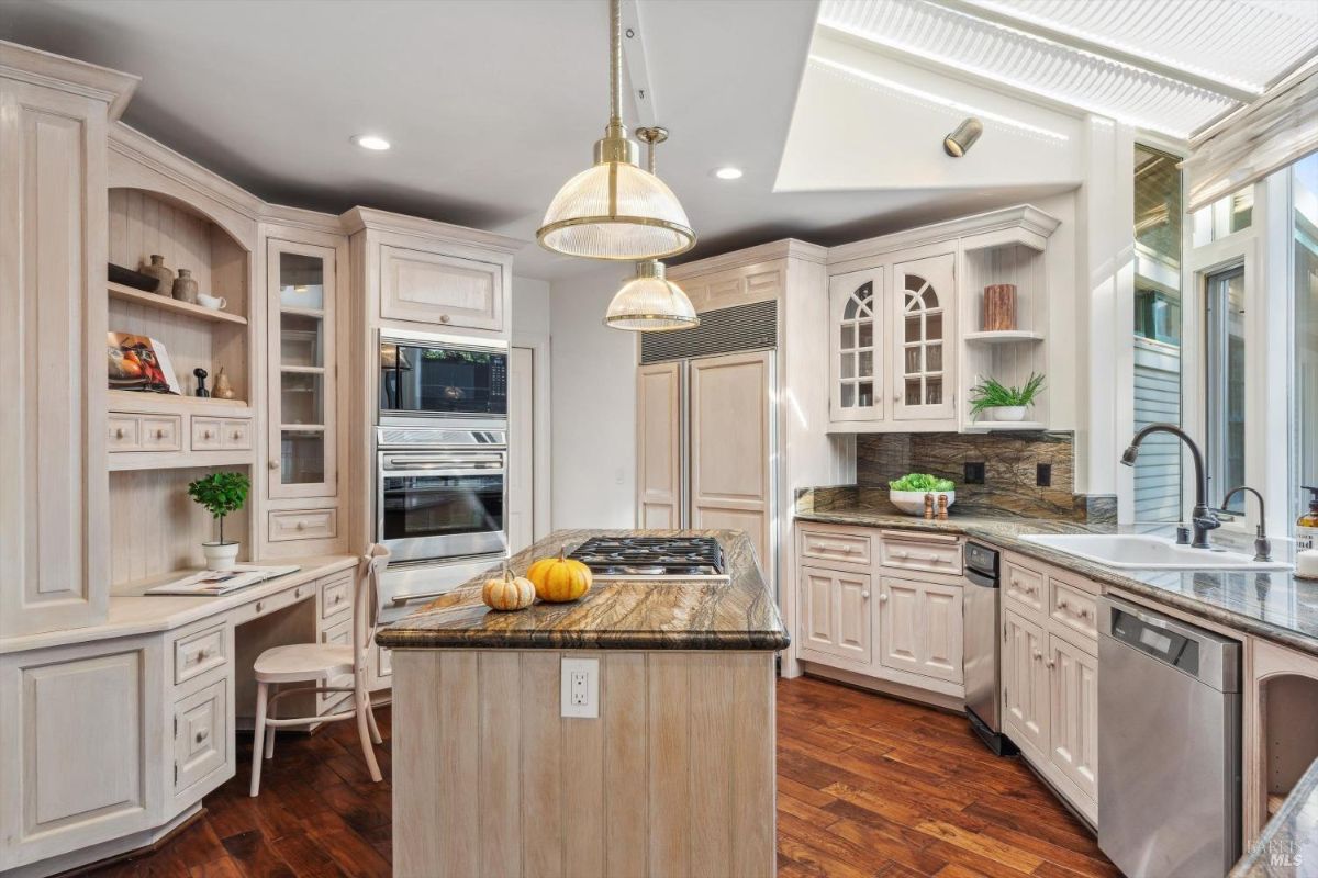 Open kitchen featuring light wood cabinets, granite countertops, and pendant lighting over a central island with a cooktop.