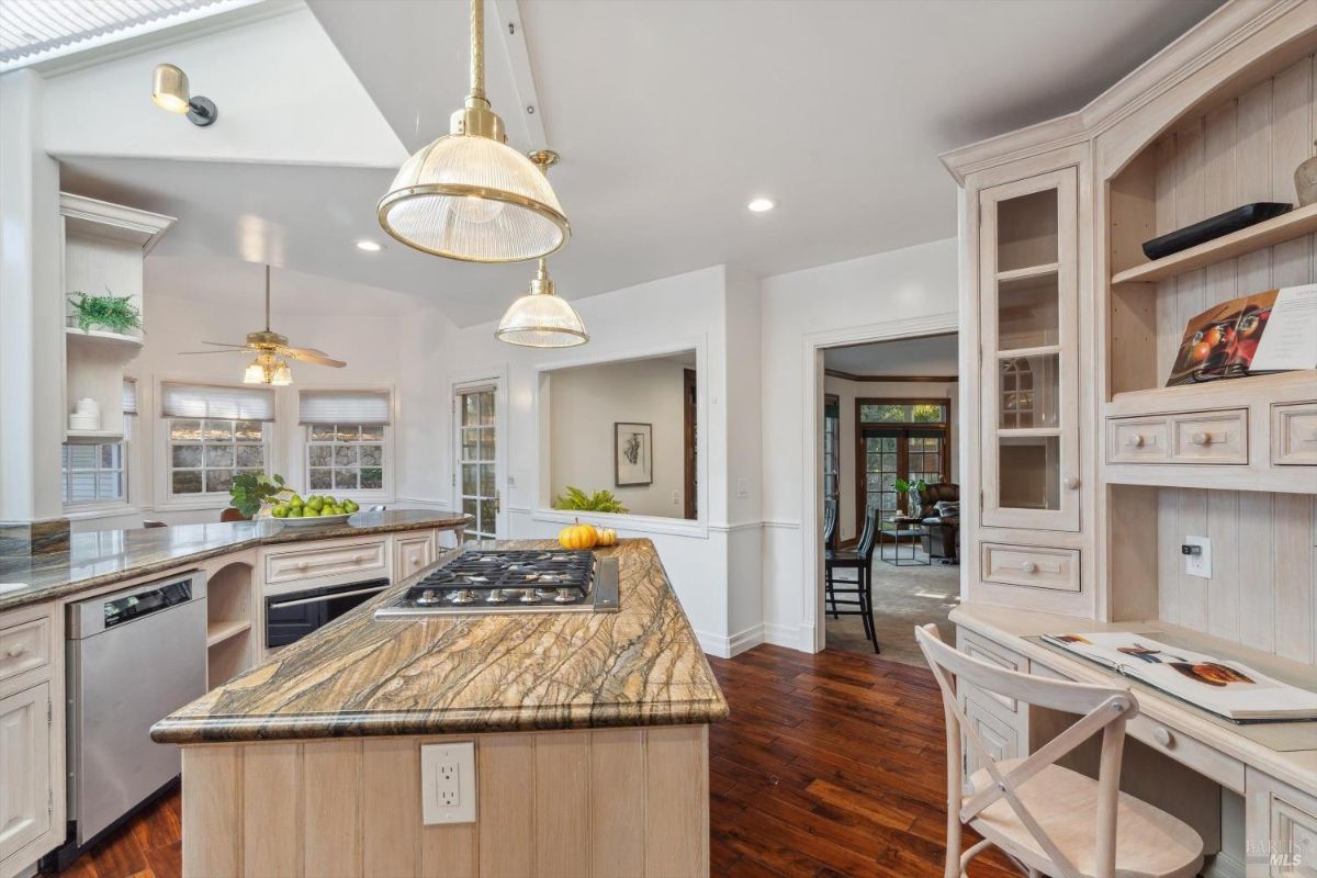 Kitchen area with a curved island, gas cooktop, and built-in workspace, adjoining a sunlit breakfast nook.