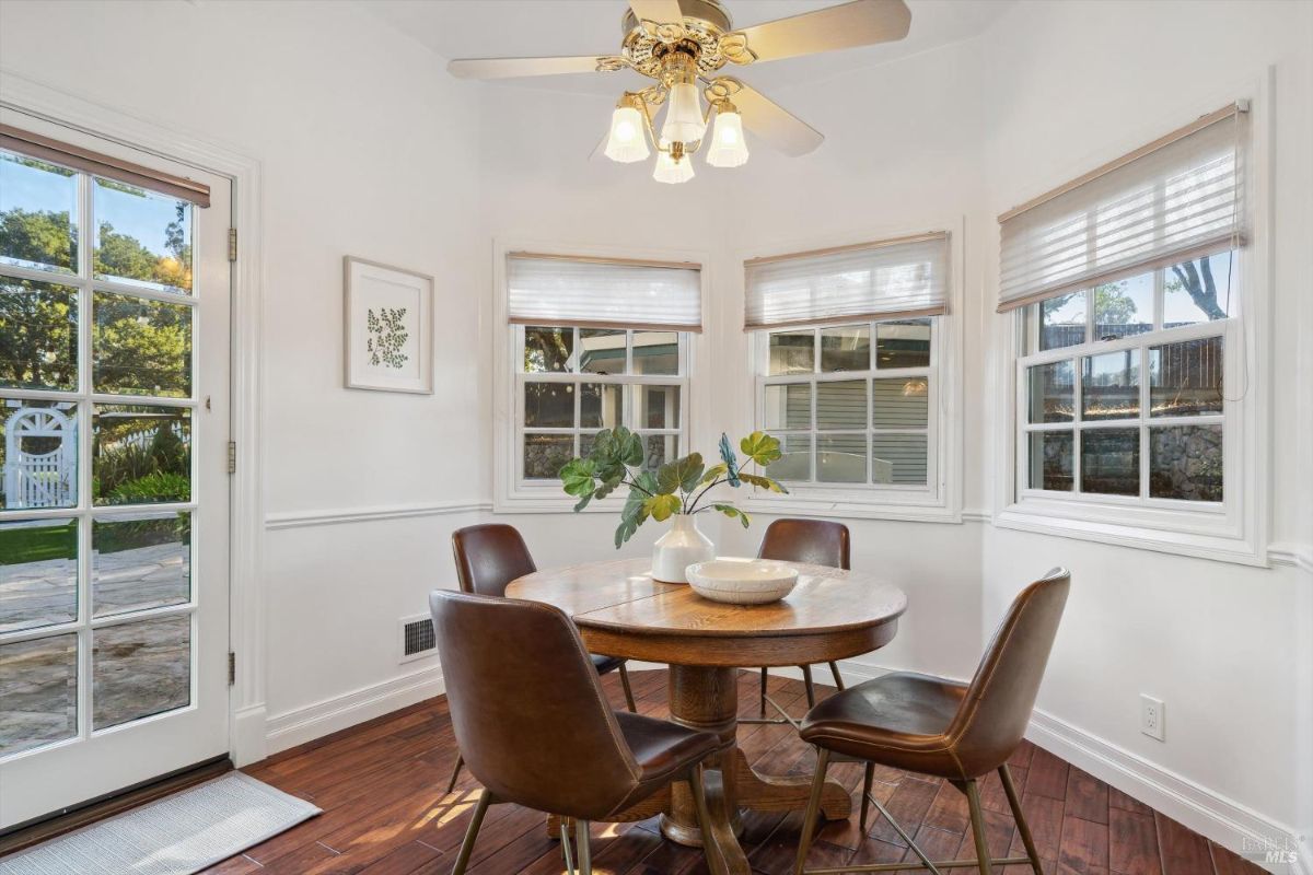 Small breakfast nook or dining area with a round wooden table with four chairs, a ceiling fan, and multiple windows offering views of the outdoors.