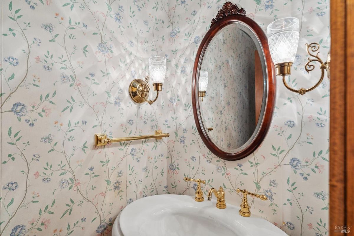 Powder room with floral wallpaper, a vintage-style oval mirror, and gold fixtures.