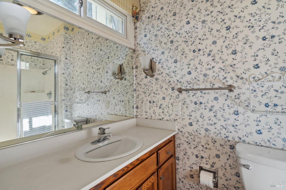 Bathroom with a single sink vanity, floral wallpaper, and a glass-enclosed shower.