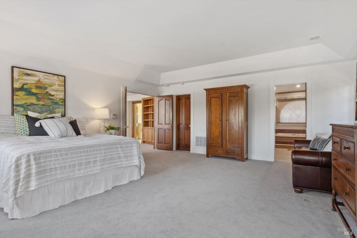 Spacious bedroom with carpet flooring, wooden furniture, and an adjoining hallway to other rooms.
