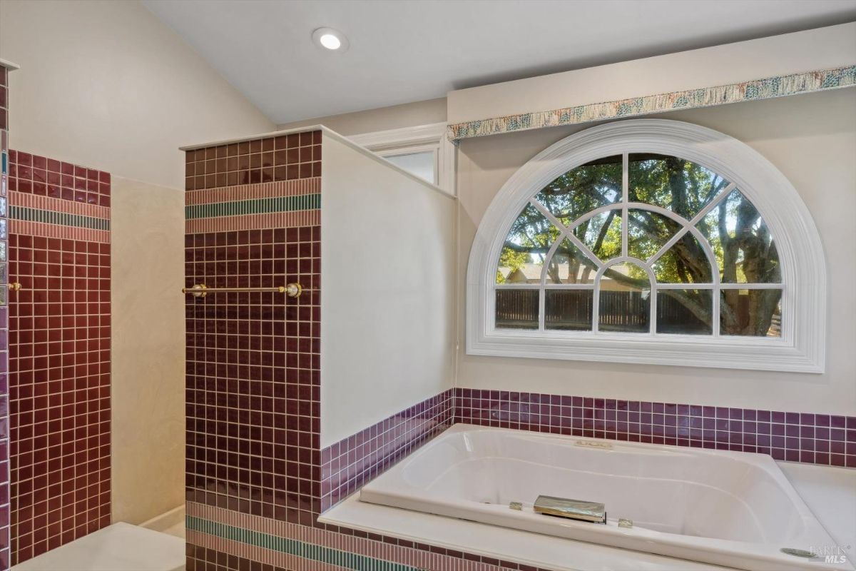 Bathroom with a corner bathtub, purple tile walls, and an arched window overlooking trees.