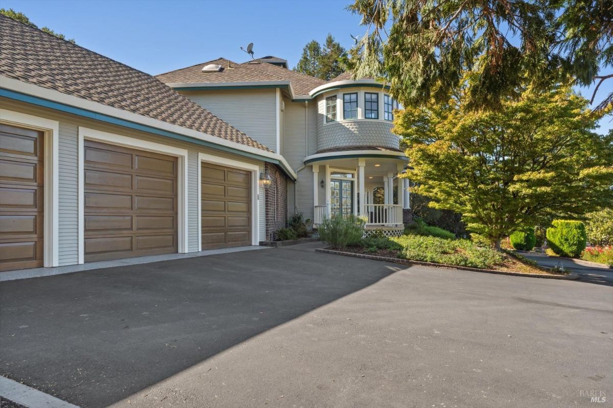 Front view of a house with a three-car garage, a circular porch, and a driveway surrounded by trees.
