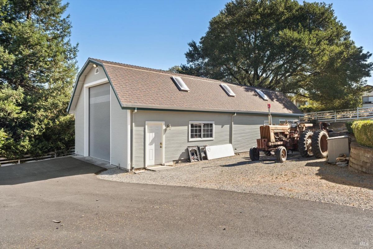Detached barn-style building with skylights, a large roll-up door, and a paved driveway area.