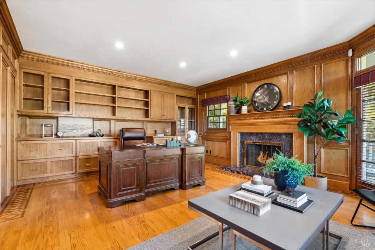 The room features a large desk, built-in bookshelves, a fireplace, and hardwood floors.