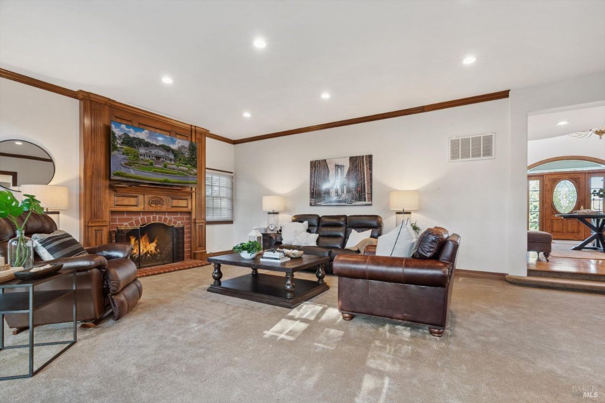 Spacious living room with a fireplace, a large TV mounted above it, and a seating area with leather couches and a coffee table.