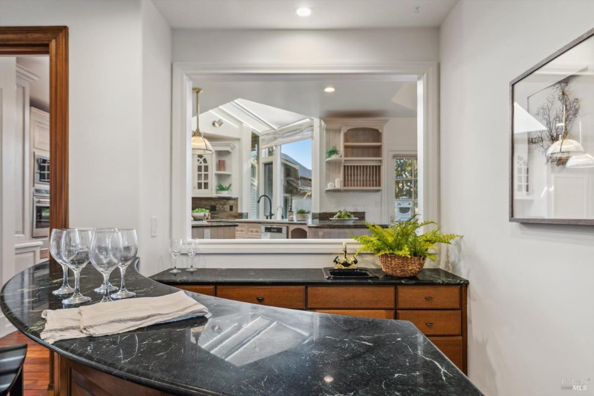Bar area with dark stone countertops and a window opening into the kitchen.
