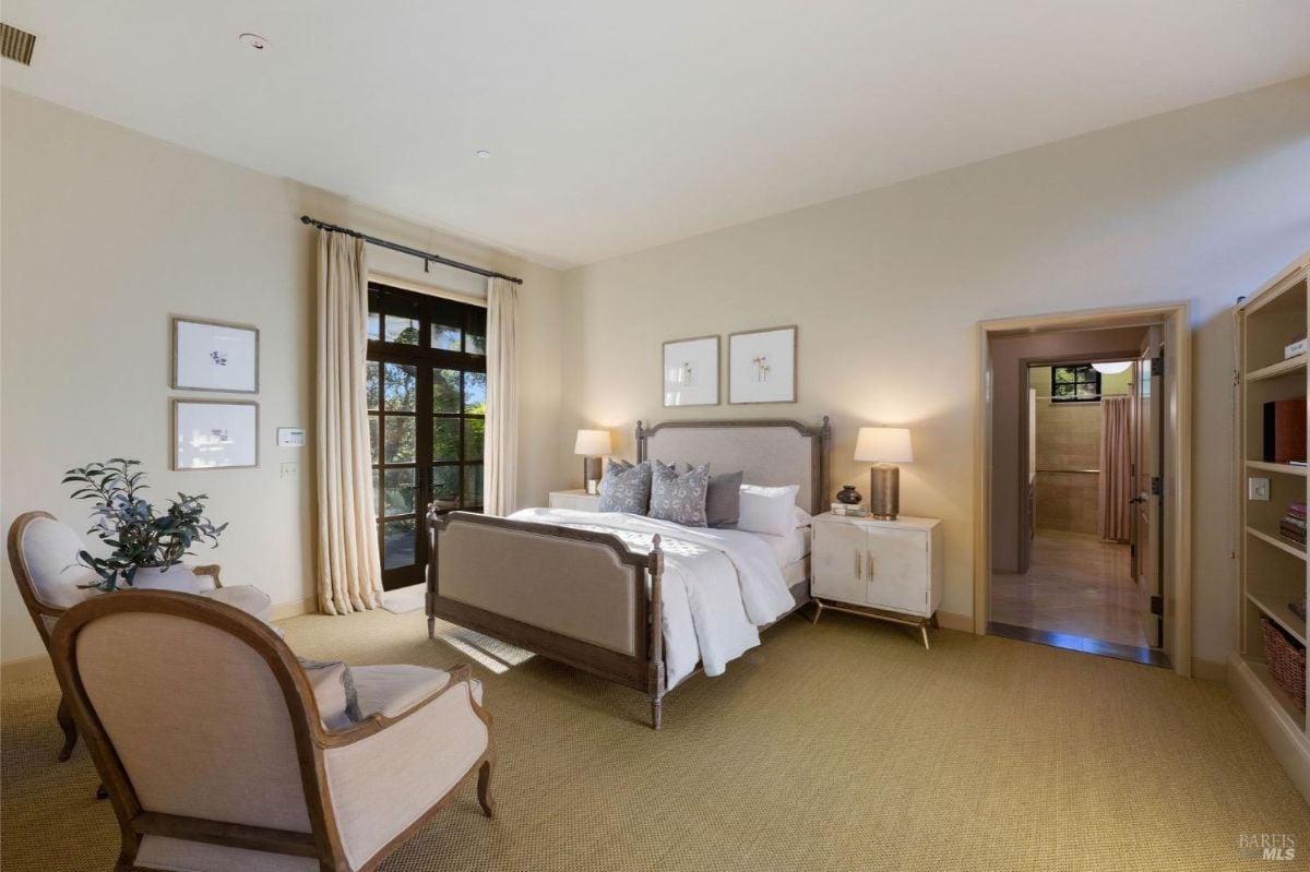 Bedroom with a large bed, armchairs, and access to a private balcony or outdoor view through French doors.