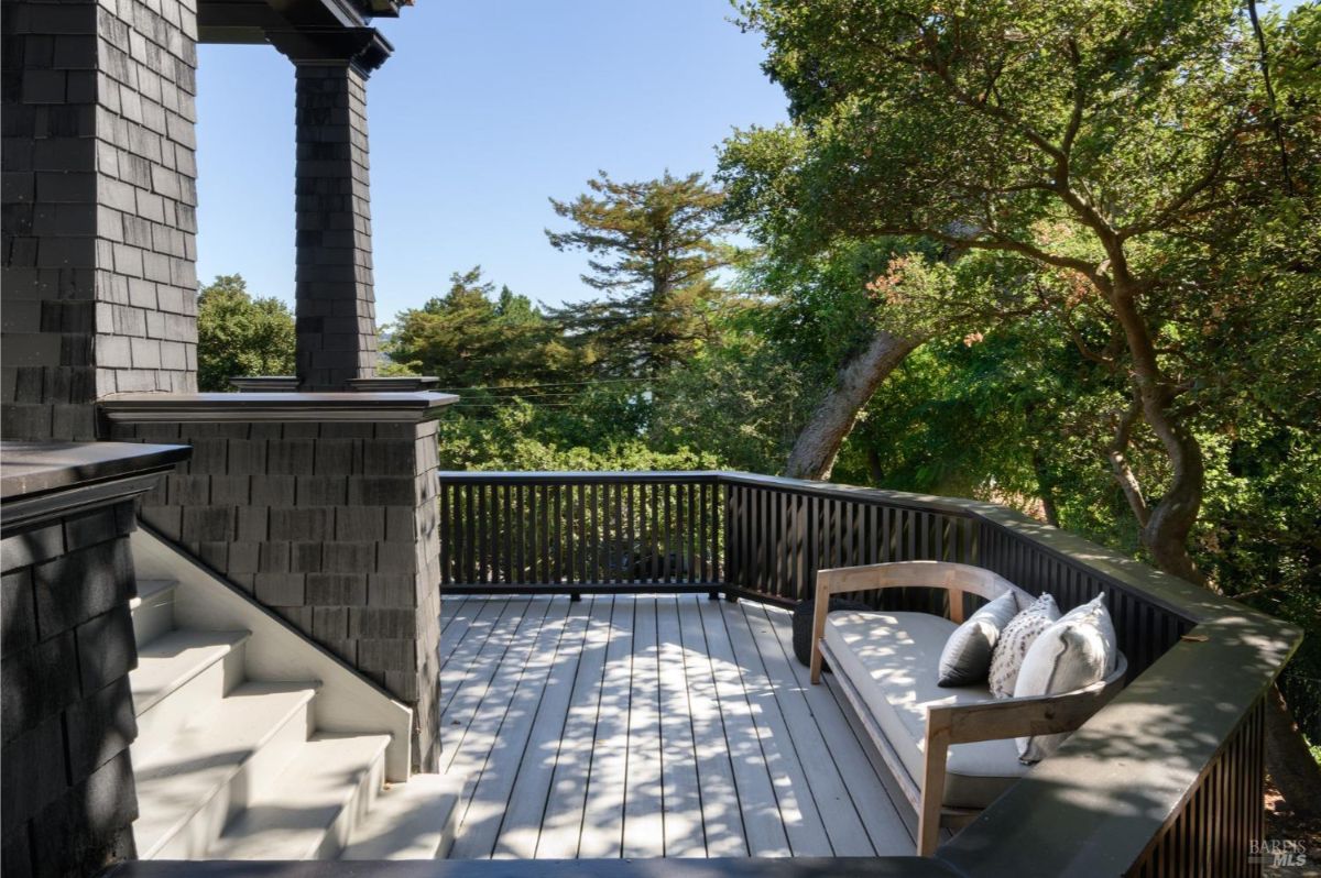 Deck with dark siding, a wooden bench, and a view of trees and water.