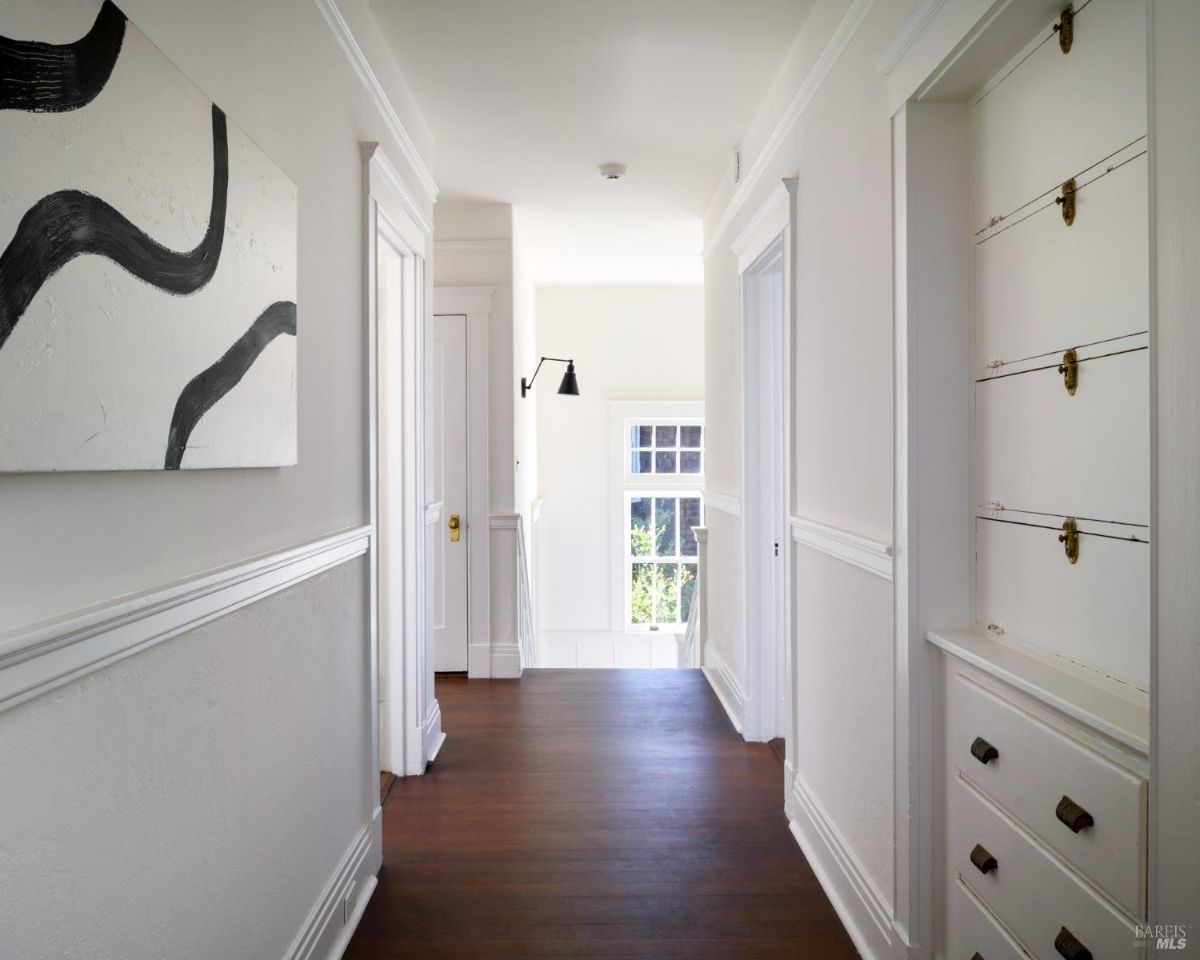 Hallway has white wainscoting, wood floors, built-in shelving, and artwork.
