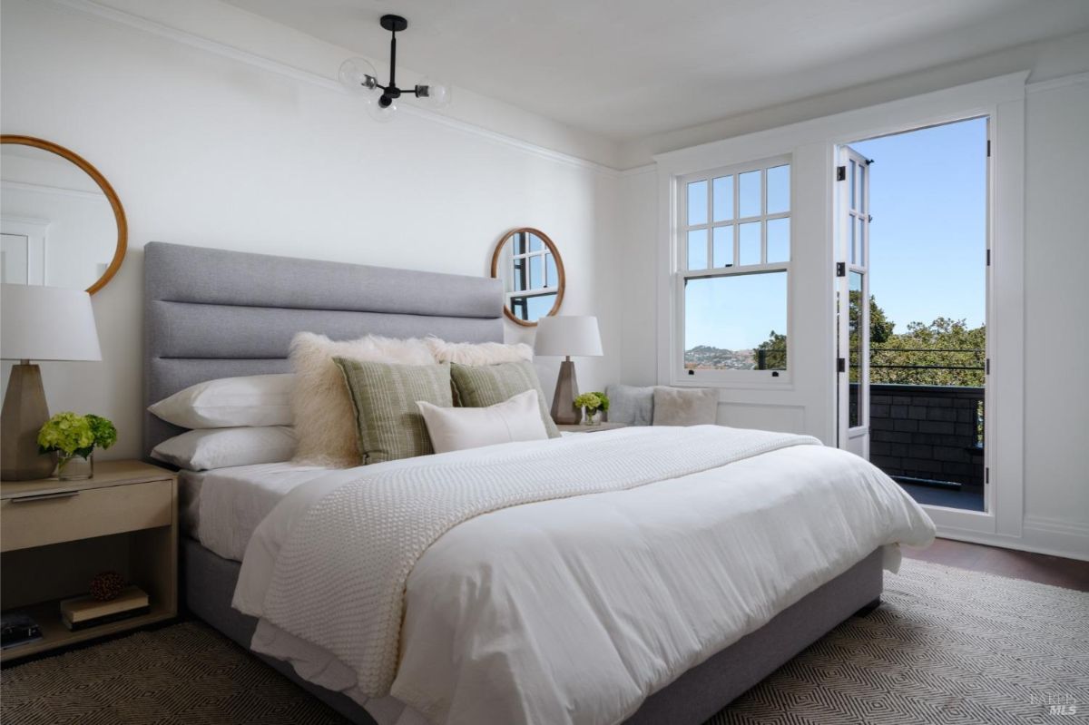  Bedroom with a gray upholstered headboard, white walls, and a door leading to a balcony with a view.