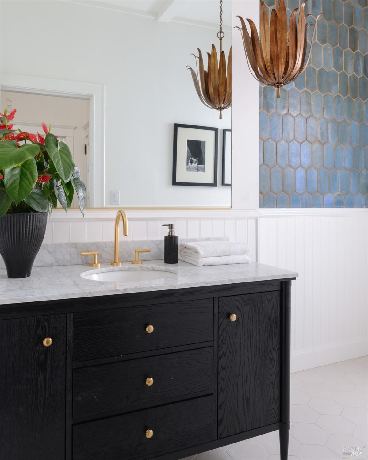 Bathroom has a black vanity with marble countertop, gold fixtures, and blue tiled wall.