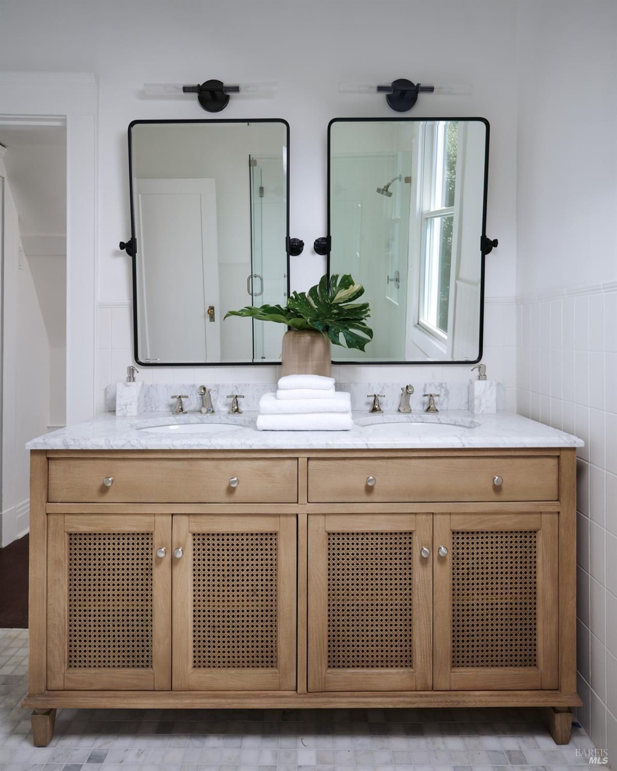 Bathroom with a double vanity, two mirrors, and a light wood vanity with cane doors.