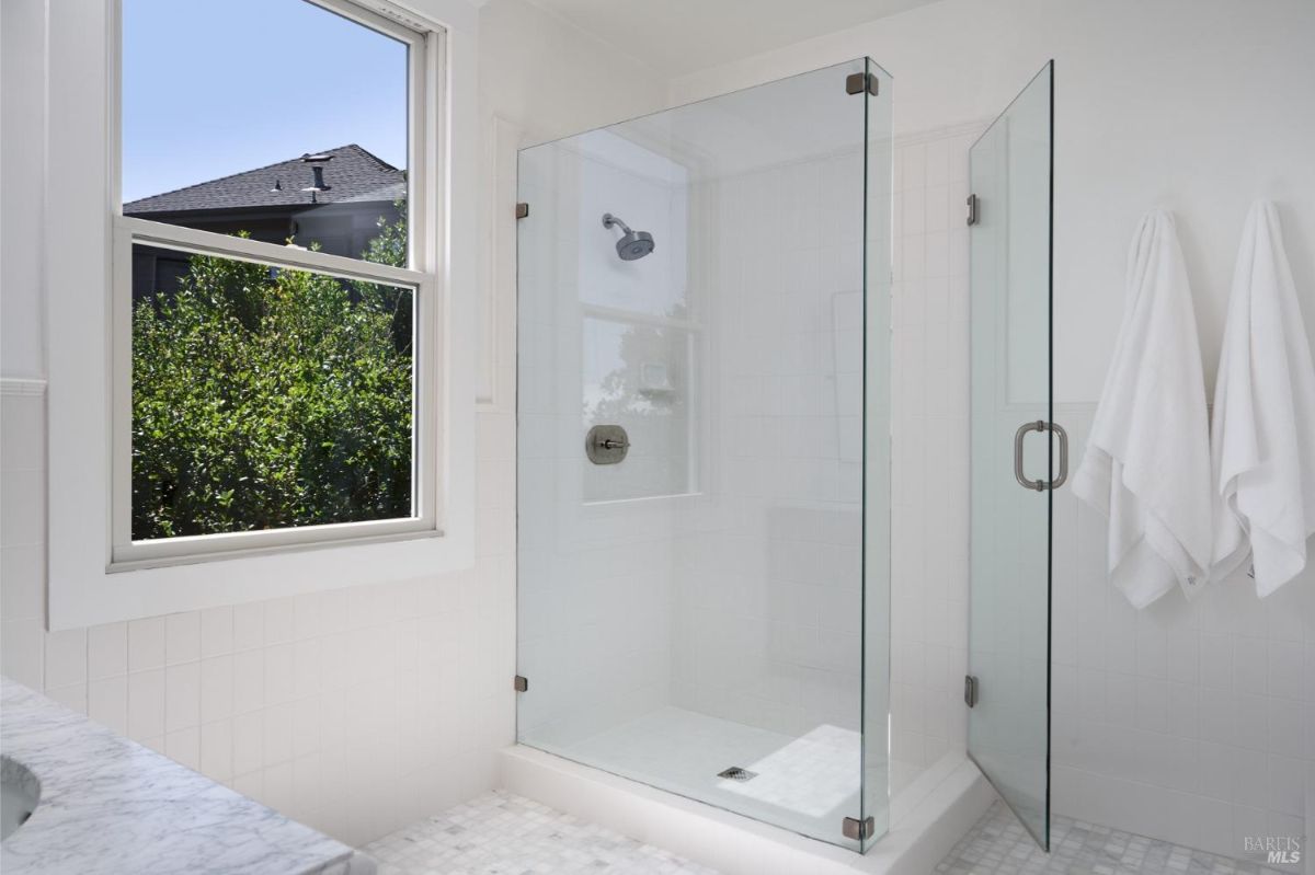 Bathroom with white walls, a window, and a glass-enclosed shower.