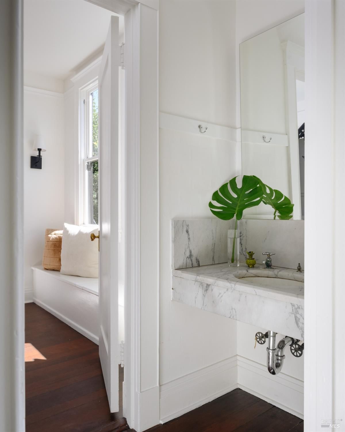 Small bathroom has a window seat, marble sink, and a large mirror.