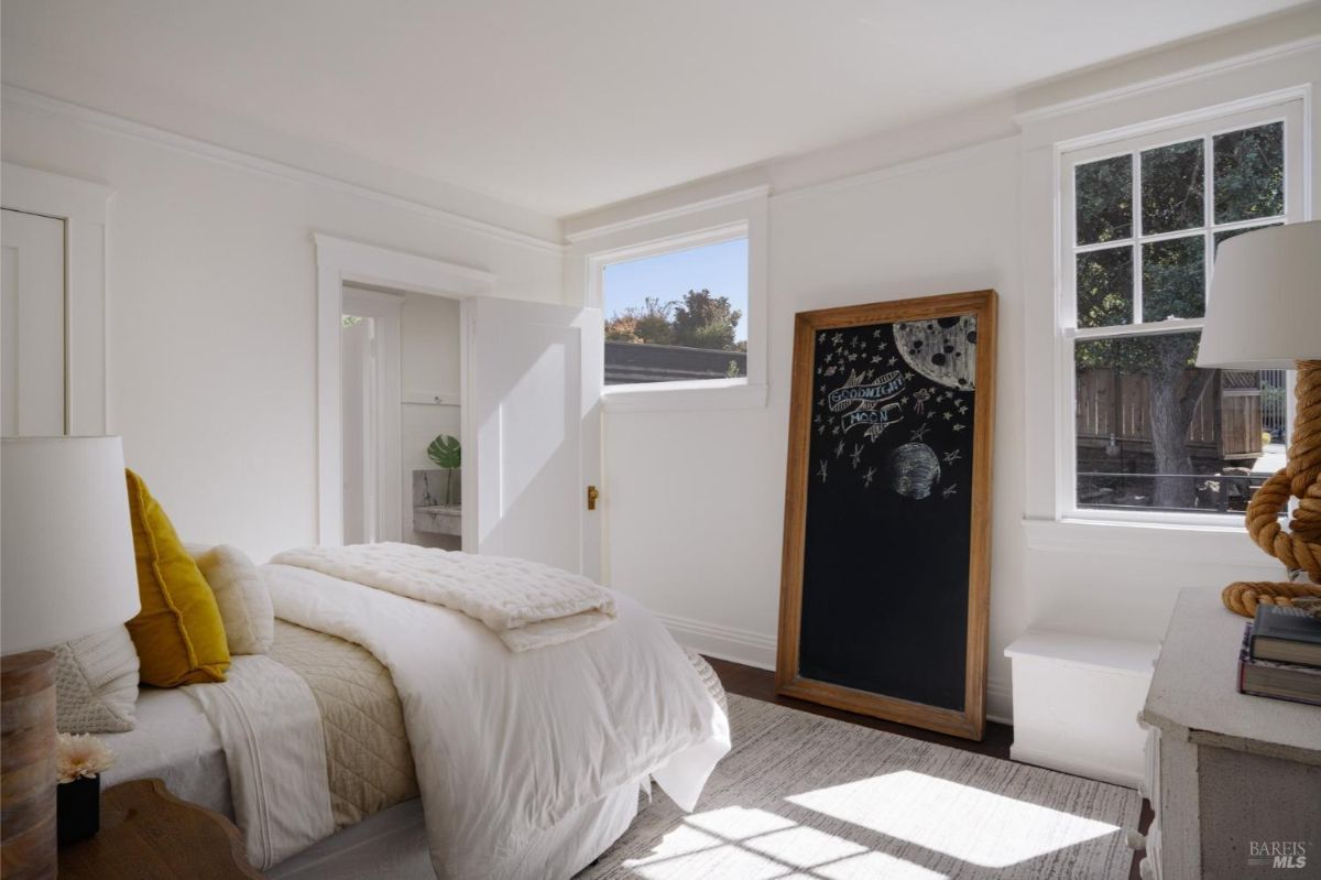 Bedroom with white walls, two windows, and a chalkboard with a drawing of the moon.