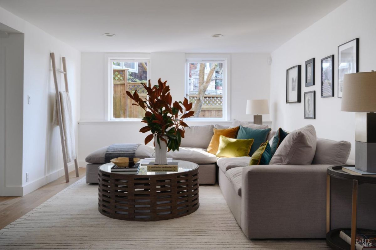 Cozy living room with a sectional sofa, colorful cushions, and two windows providing natural light.