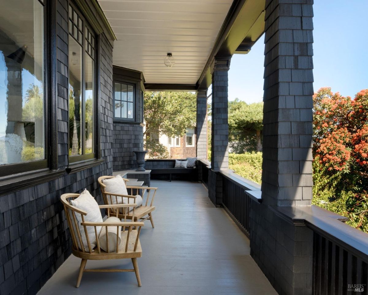 Covered porch has dark wood siding, columns, two chairs, and a built-in bench.