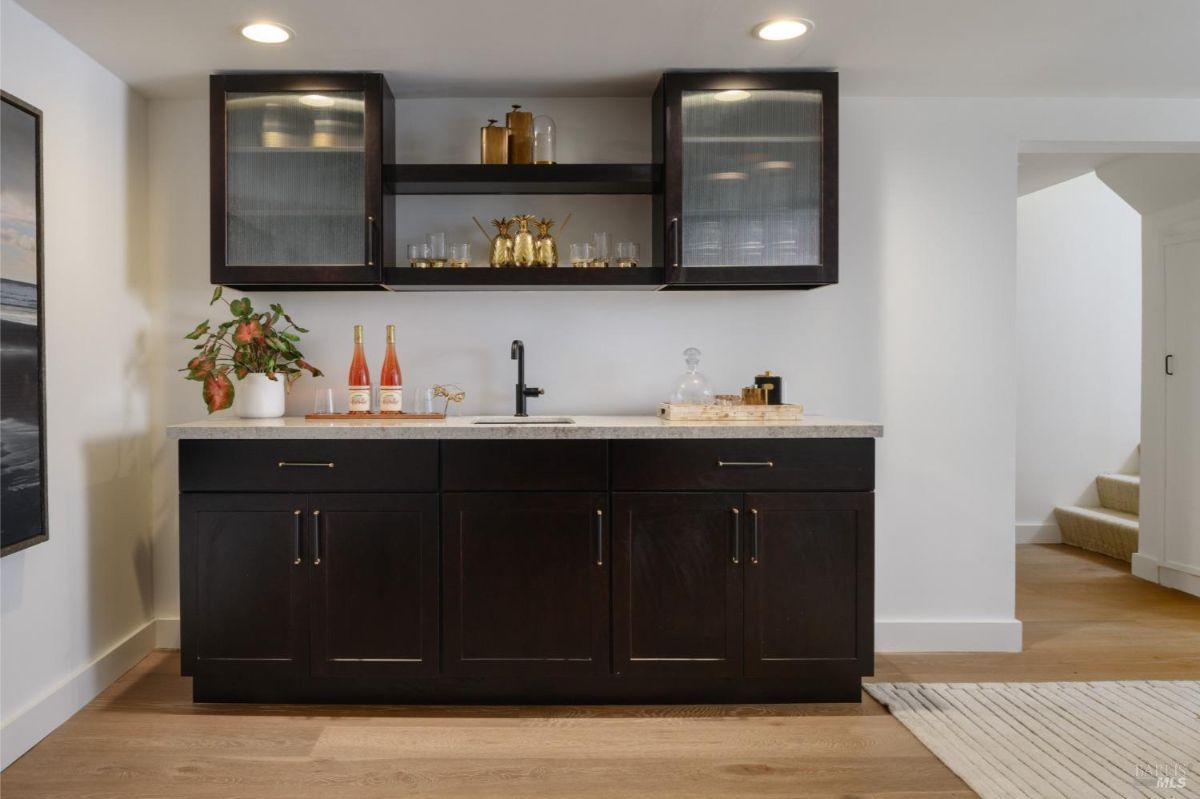 Bar area with dark cabinets, a light countertop, and glass-fronted upper cabinets.
