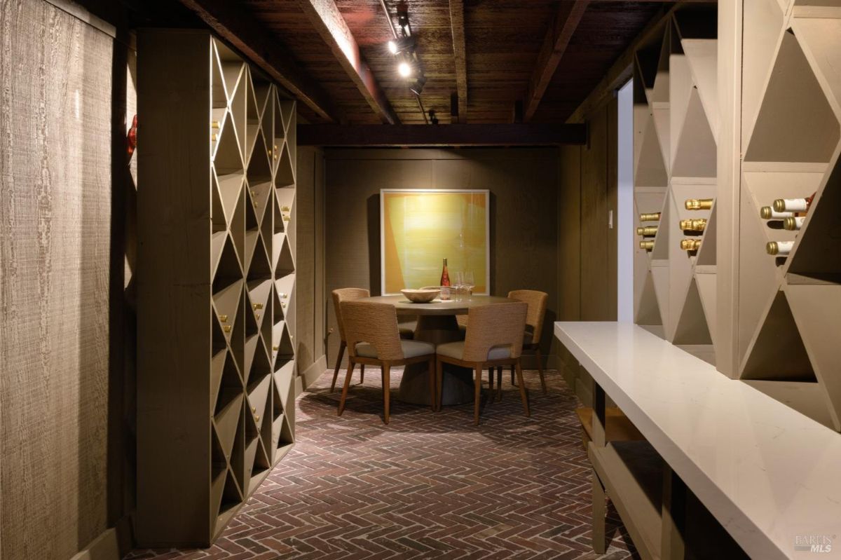 Wine cellar has wood ceiling, wine racks, a small table with chairs, and a serving counter.