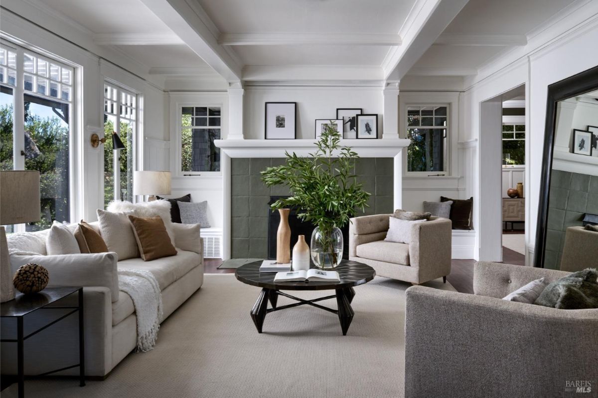 Living room with a central fireplace, coffered ceiling, and neutral-colored furniture.