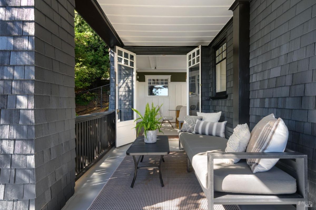  covered porch with dark siding, a gray couch, and a small table.