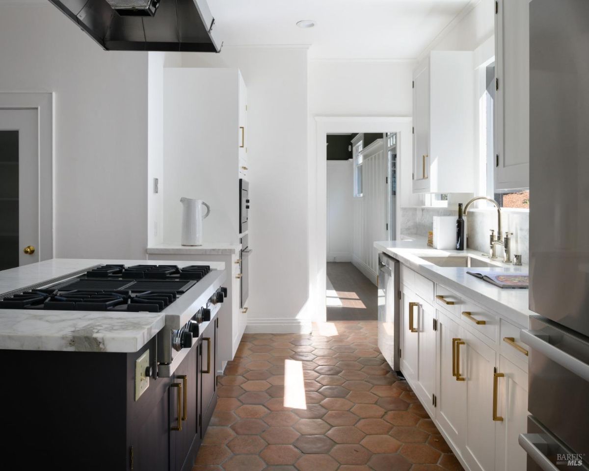 Kitchen with white cabinets, dark countertops, a stainless steel range hood, and terracotta floor tiles.