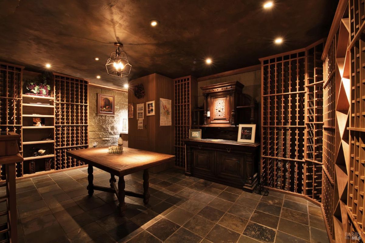 Wine cellar with extensive wooden racking for wine bottles, a tasting table, and a stone accent wall.