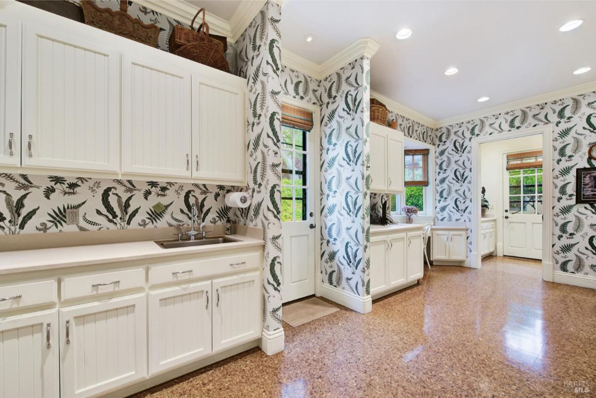 Laundry room boasts ample counter space, white cabinetry, and eye-catching botanical wallpaper.