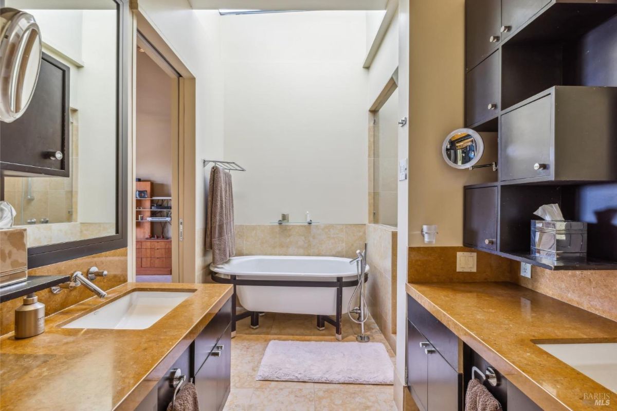 Modern bathroom with a freestanding bathtub and dark wooden cabinets under a skylight.