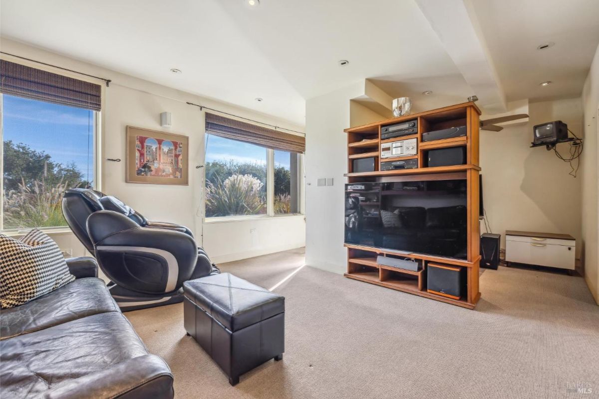 Home theater with leather seating, built-in media shelves, and natural light from windows.