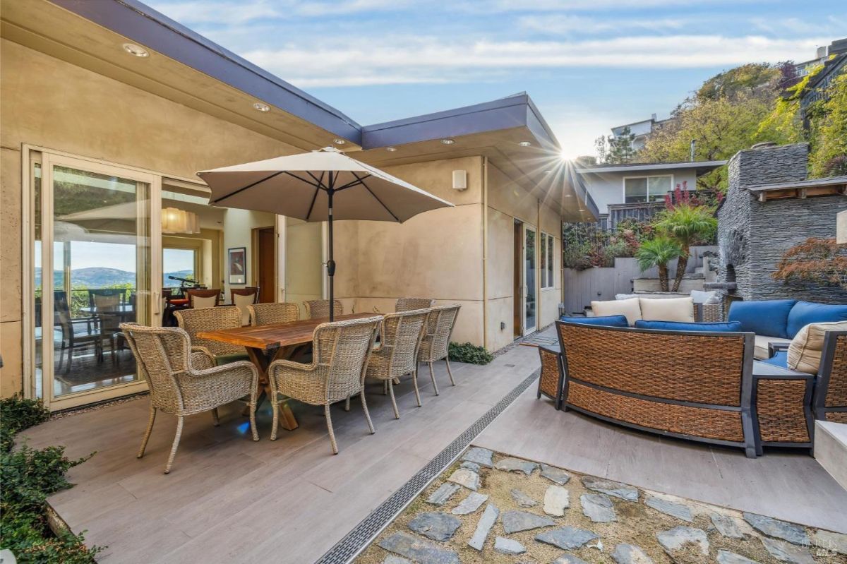 Outdoor space with a dining table, an umbrella, and seating area against a hillside landscape.