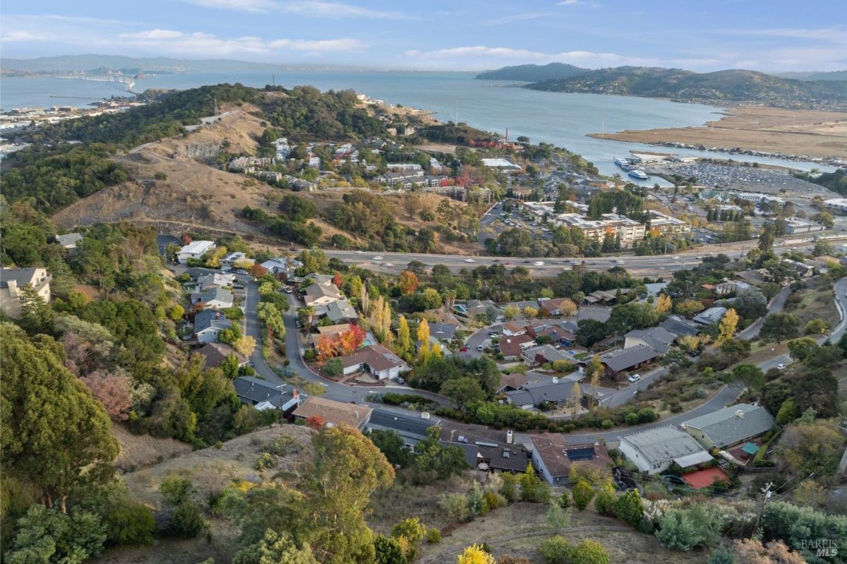 Aerial view of a residential area with hills and a water body in the background.