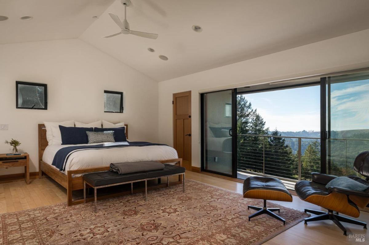 A bedroom with bed, a sliding door to a balcony, and forest views.