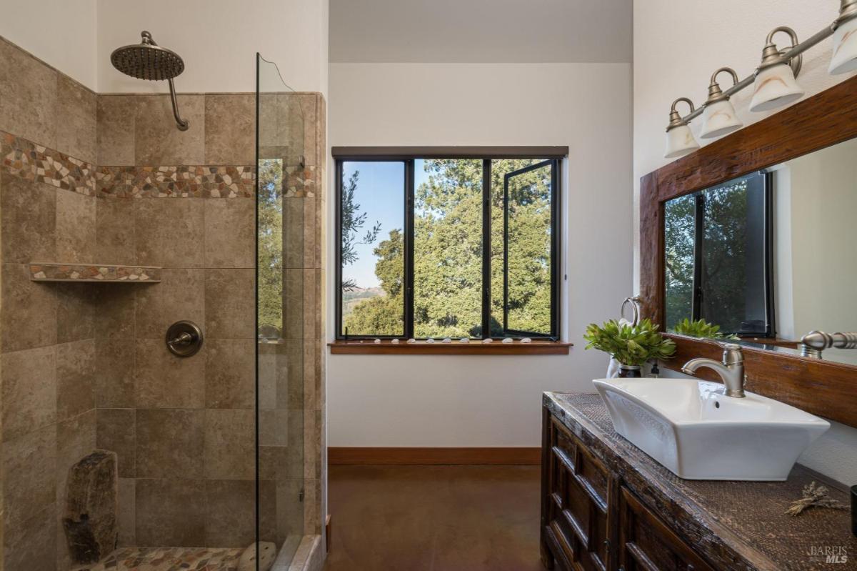 Bathroom with a tiled shower, large window, and vanity.