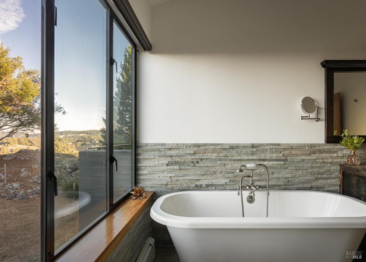Bathroom with a freestanding bathtub and large windows.